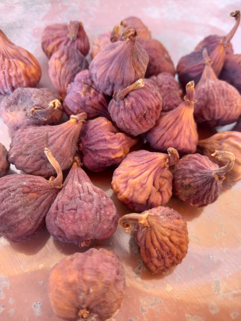 Suszone figi o pomarszczonej skórce w odcieniach fioletu i brązu, ułożone na lekko zabrudzonej powierzchni