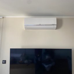 Top Klima - Biały klimatyzator LG Dual Inverter zamontowany na ścianie nad telewizorem w nowoczesnym salonie.