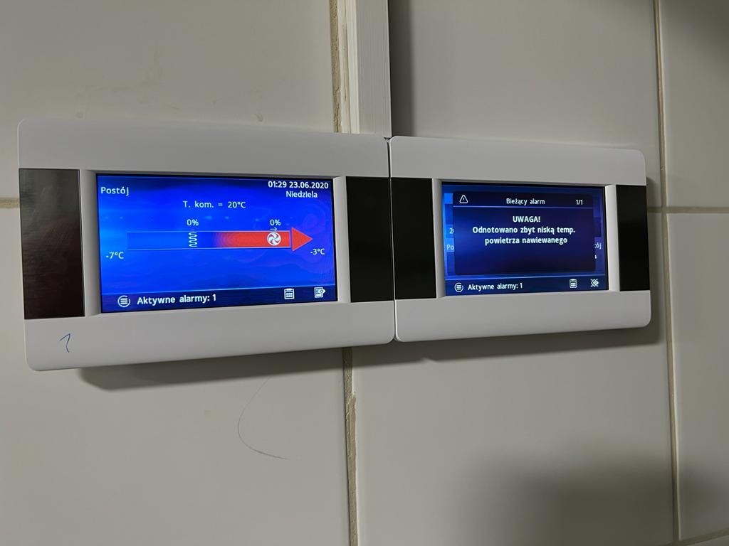 Biały panel sterowania z dwoma ekranami LCD zamontowany na kafelkowanej ścianie, wyświetlający informacje o temperaturze i alarmach, z widoczną datą 23.06.2020 i komunikatem o zbyt niskiej...