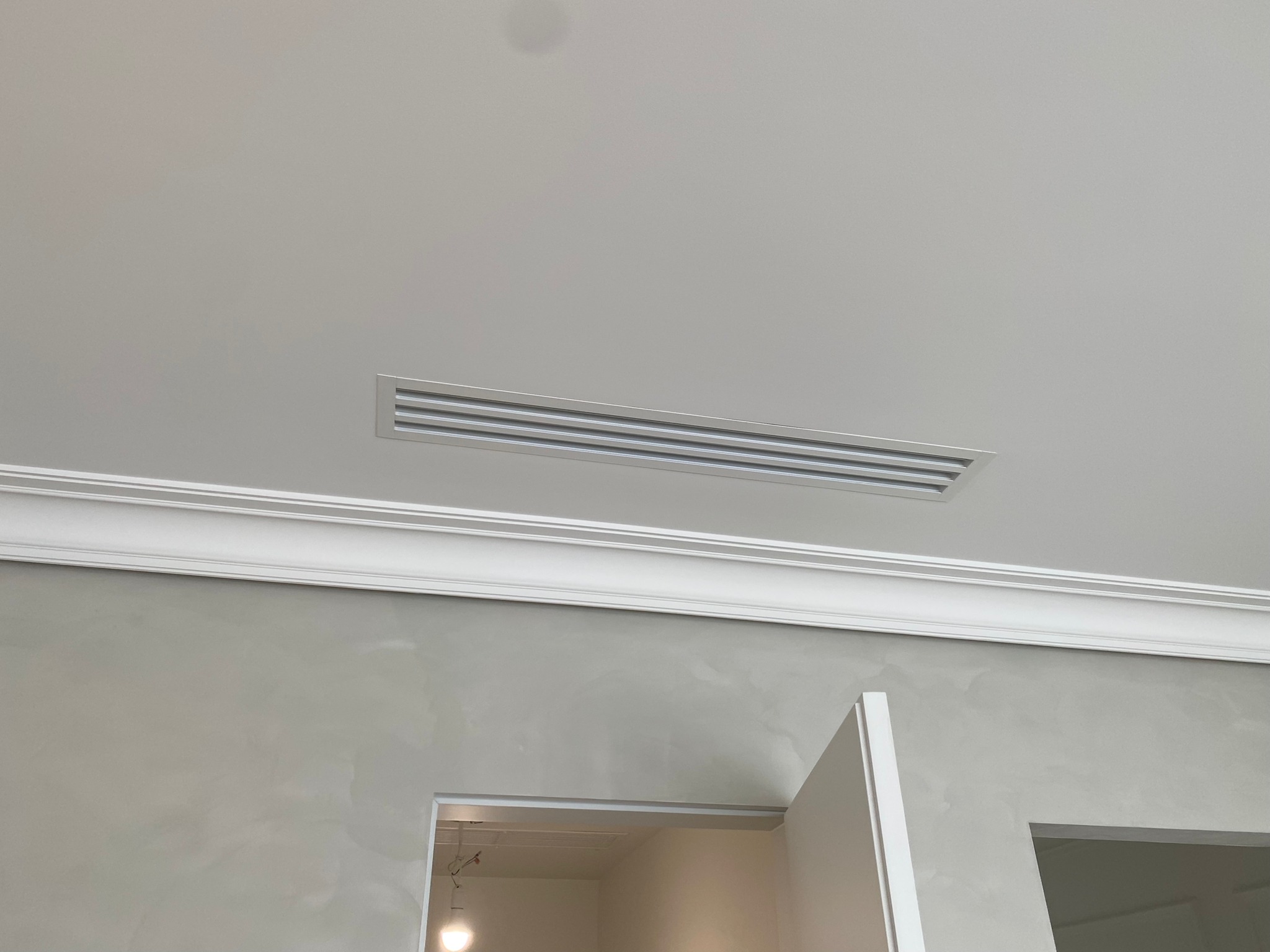 Szary sufit z prostokątną kratką wentylacyjną, ozdobiony listwą przysufitową, widoczne wejście do pomieszczenia