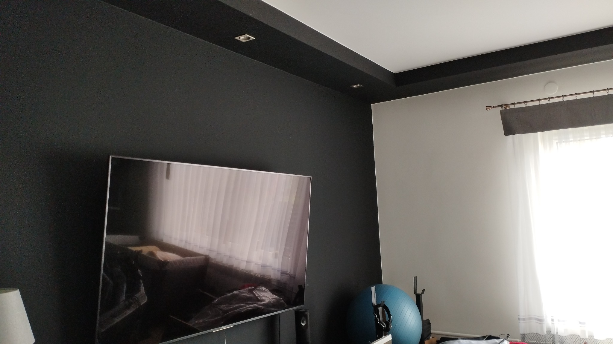 Pokój po remoncie: czarna ściana kontrastuje z białą, sufit z czarnymi elementami, duży telewizor, piłka do ćwiczeń.