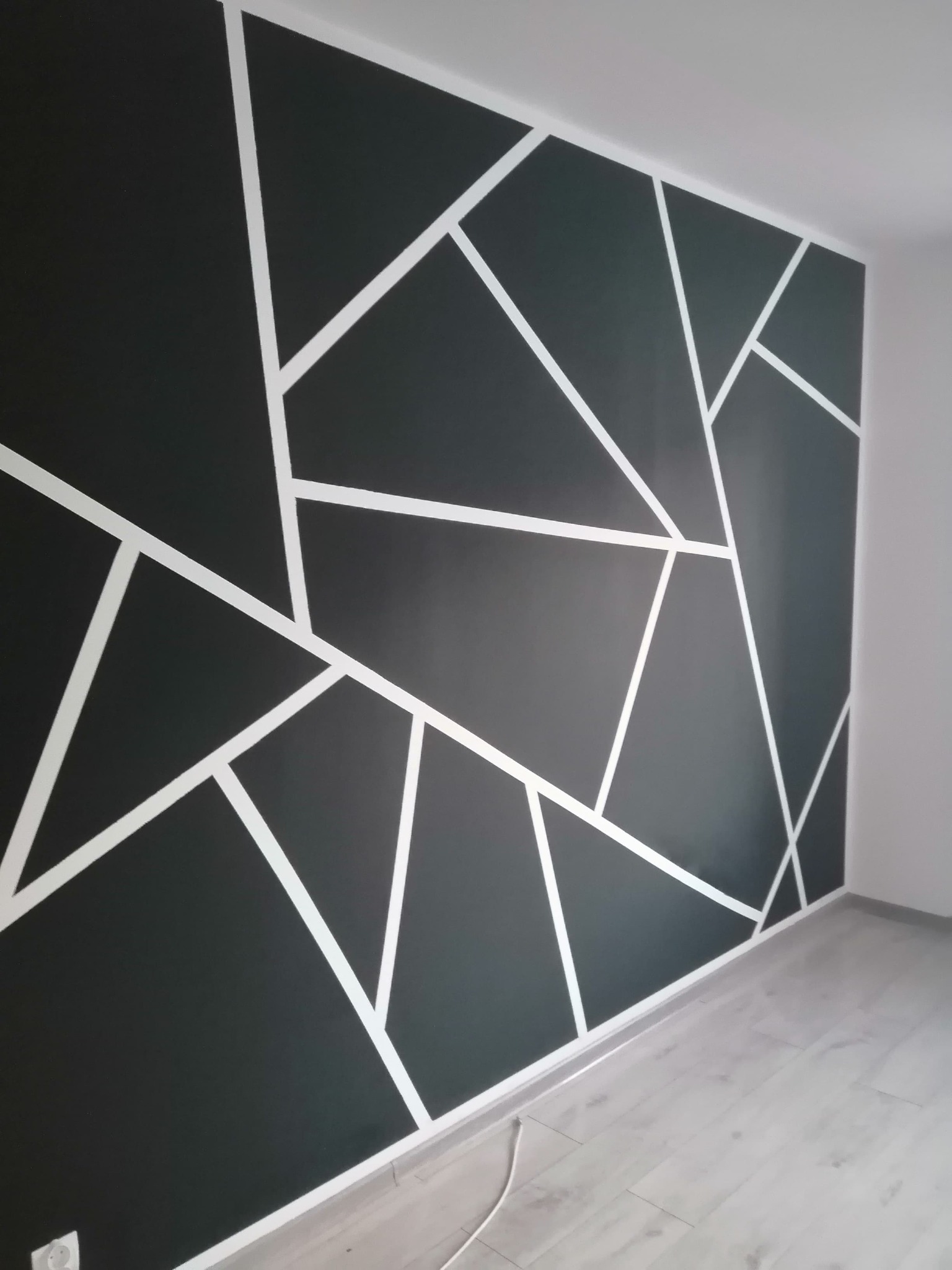 Ściana pomalowana na grafitowo z białymi geometrycznymi wzorami tworzącymi abstrakcyjny design.