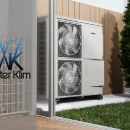 Biała pompa ciepła z dwoma wentylatorami na zewnątrz budynku, widoczna przez szklane drzwi przesuwne; po lewej logo Winter Klim na tle kratownicy.