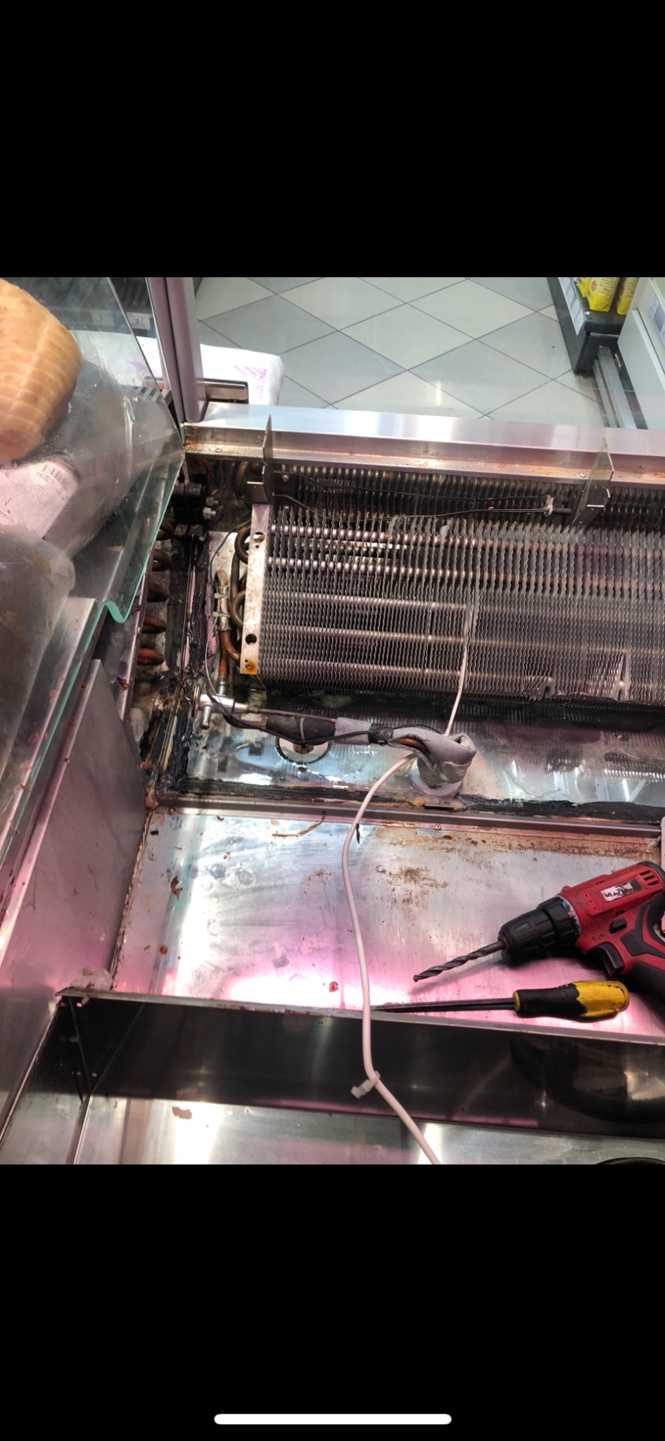 Wnętrze chłodniczej lady sklepowej w trakcie naprawy, widoczny parownik, przewody, wkrętarka akumulatorowa i śrubokręt.