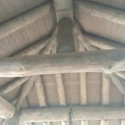 Wnętrze drewnianej konstrukcji dachu z okrągłymi belkami, widok od dołu, z widocznymi elementami więźby dachowej i deskowaniem.