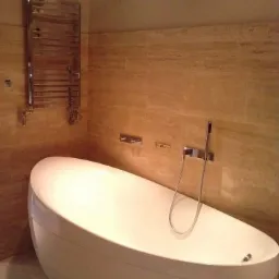 Nowoczesna łazienka z wolnostojącą białą wanną owalną, beżowe płytki na ścianach, chromowany grzejnik drabinkowy i armatura.