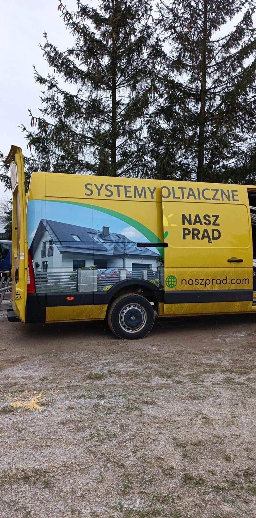 Żółty samochód dostawczy z reklamą firmy oferującej systemy fotowoltaiczne, na boku pojazdu grafika domu z panelami słonecznymi na dachu i napis 'SYSTEMY OLTAICZNE NASZ PRĄD naszprad.com'