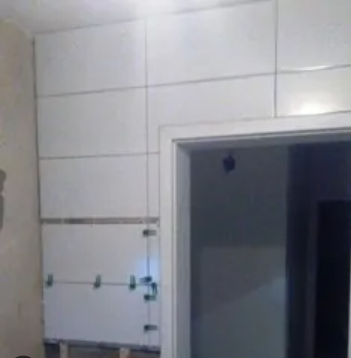 Białe płytki ceramiczne układane na ścianie w trakcie remontu, widoczne klipsy dystansowe i fragment futryny drzwi.