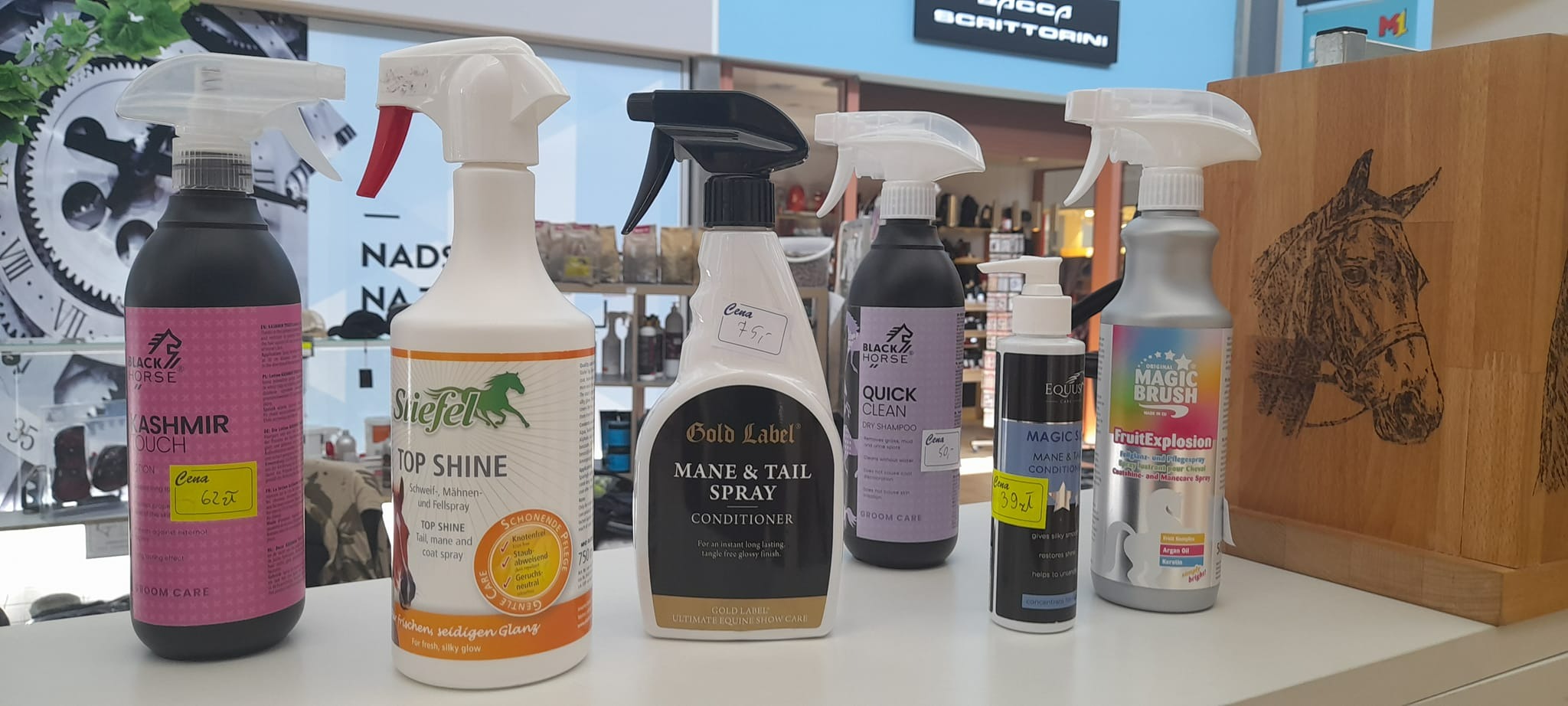 Różne butelki i pojemniki ze środkami do pielęgnacji koni, w tym szampony, odżywki i spraye do sierści, ustawione obok siebie na półce w sklepie zoologicznym, z cenami na żółtych naklejkach.