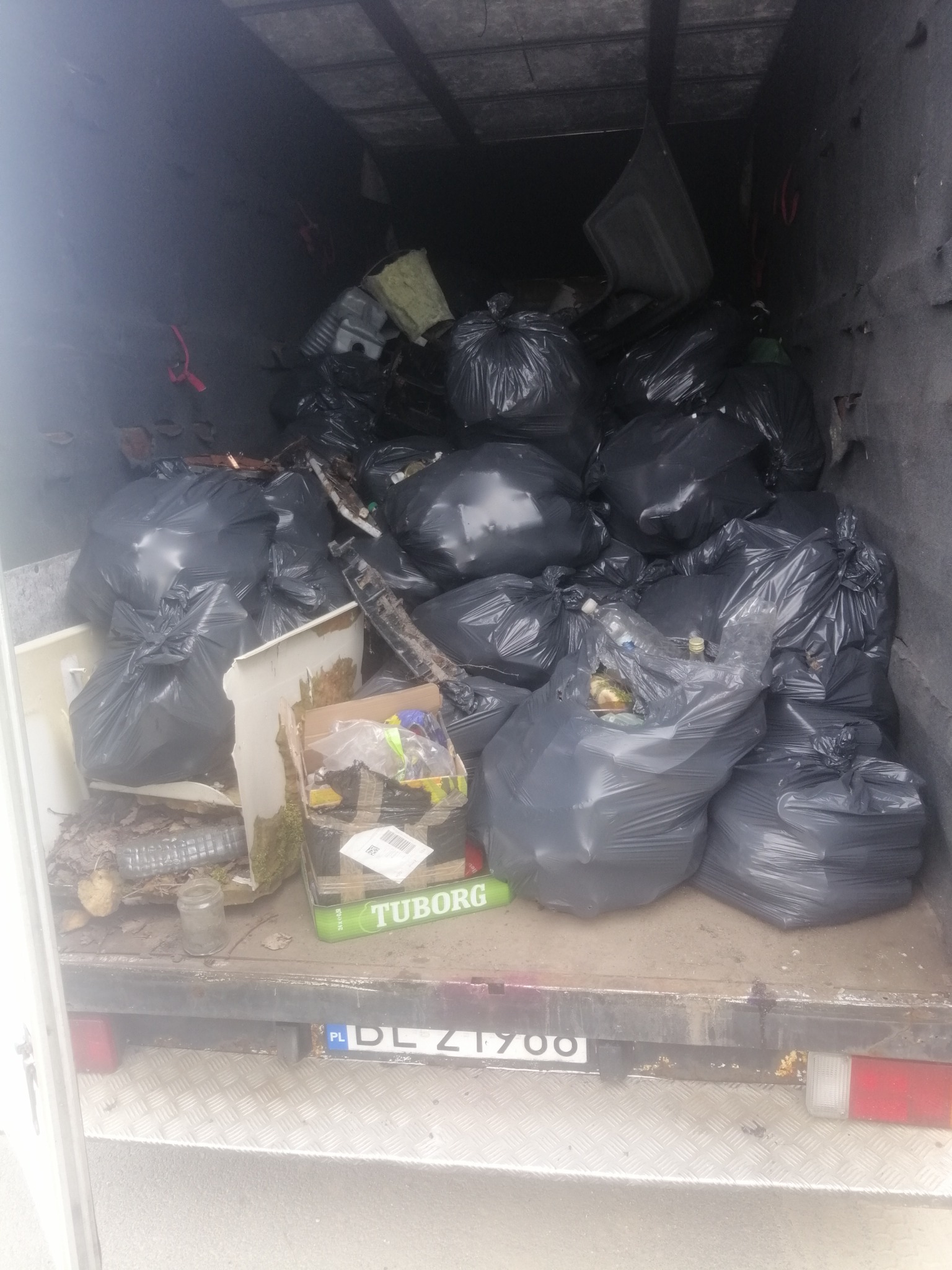 Wnętrze skrzyni ładunkowej wypełnione workami z gruzem i odpadami, widoczna tablica rejestracyjna pojazdu z przodu.