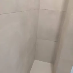 Ściany w łazience wyłożone jasnymi, matowymi płytkami ceramicznymi o dużym formacie, z widocznymi fugami, narożnik pod kątem prostym.