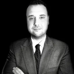 Portret mężczyzny w garniturze z założonymi rękami na czarnym tle, oświetlenie studyjne.