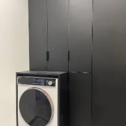 Pralka w zabudowie z czarnymi, matowymi frontami szafek, tworząca spójną całość w nowoczesnej łazience.