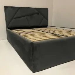 Szare łóżko tapicerowane z geometrycznym zagłówkiem i drewnianym stelażem na białym tle.