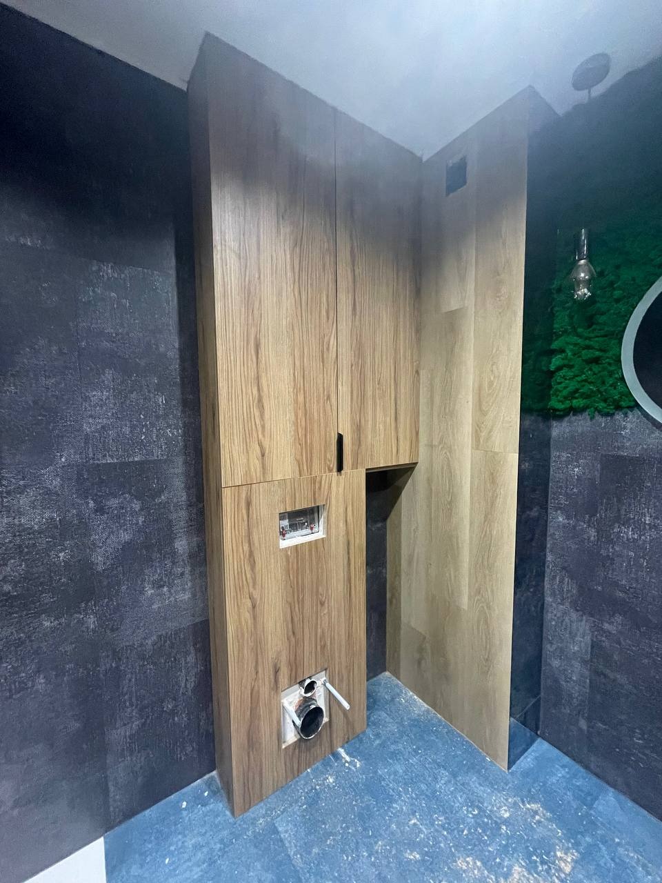 Montaż stelaża podtynkowego WC obudowanego drewnopodobną płytą meblową, widoczne przyłącza hydrauliczne i elektryczne, niebieska folia zabezpieczająca podłogę.