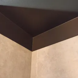 Detale wykończenia wnętrza: połączenie szarej ściany i beżowej płytki z brązowym pasem dekoracyjnym na styku.