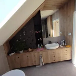 Łazienka na poddaszu w Czechowicach-Dziedzicach z zabudową meblową z drewnianym blatem pod umywalkę, czarną ścianą z półkami i lustrem.