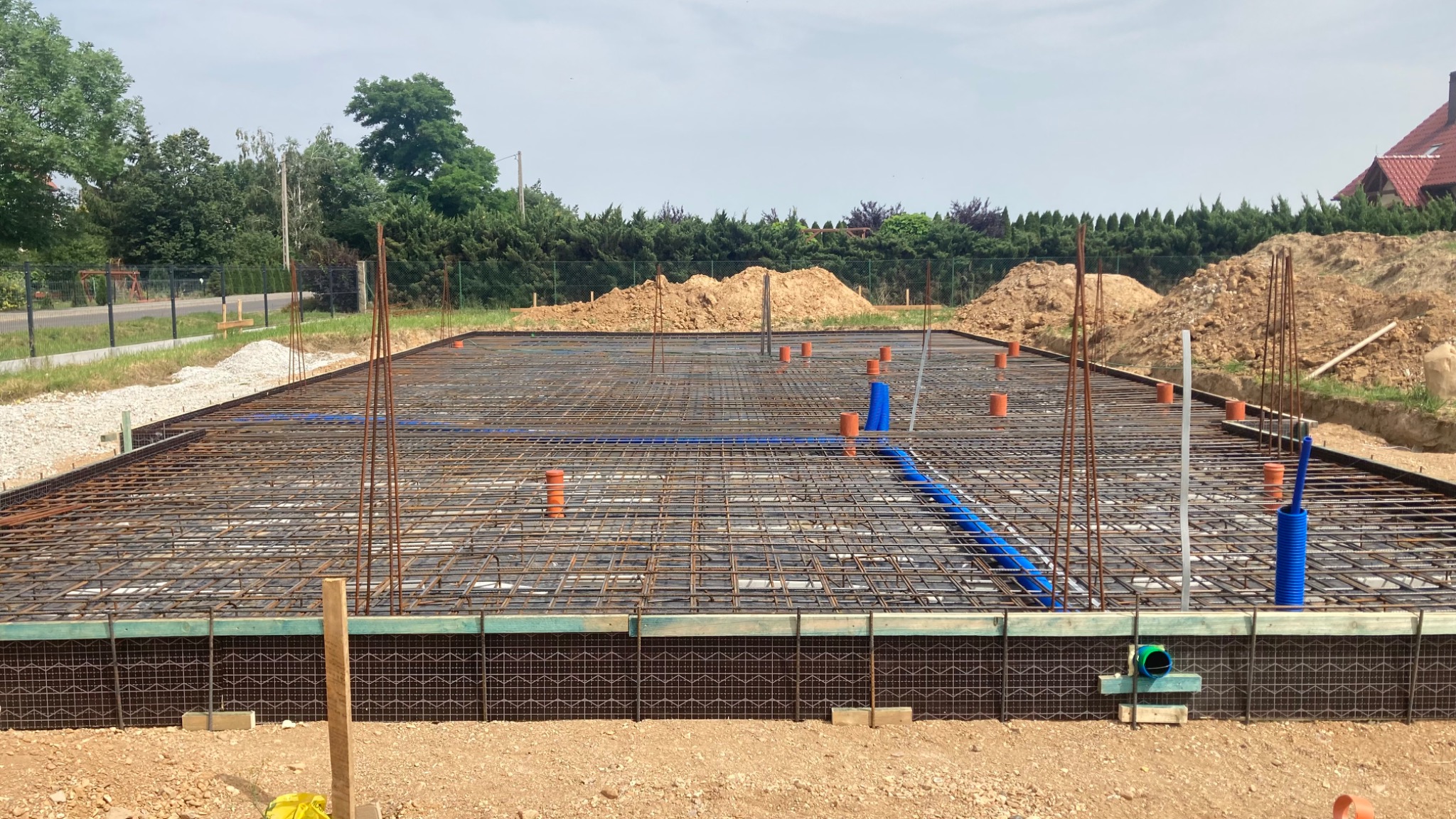 Przygotowanie zbrojenia fundamentów w Legnicy, widoczne pionowe pręty zbrojeniowe, siatka zbrojeniowa oraz instalacje sanitarne.