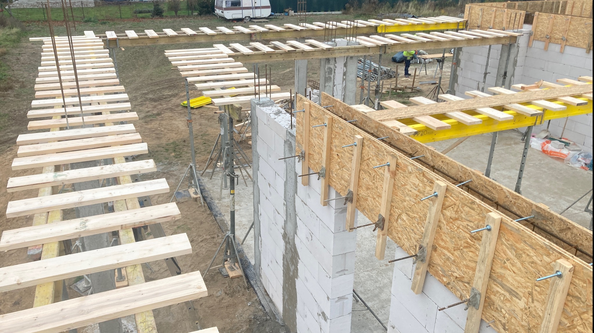 Wysoki kąt widzenia na budowę domu z betonu komórkowego z drewnianym szalunkiem i zbrojeniem, widoczne podpory i elementy konstrukcyjne.