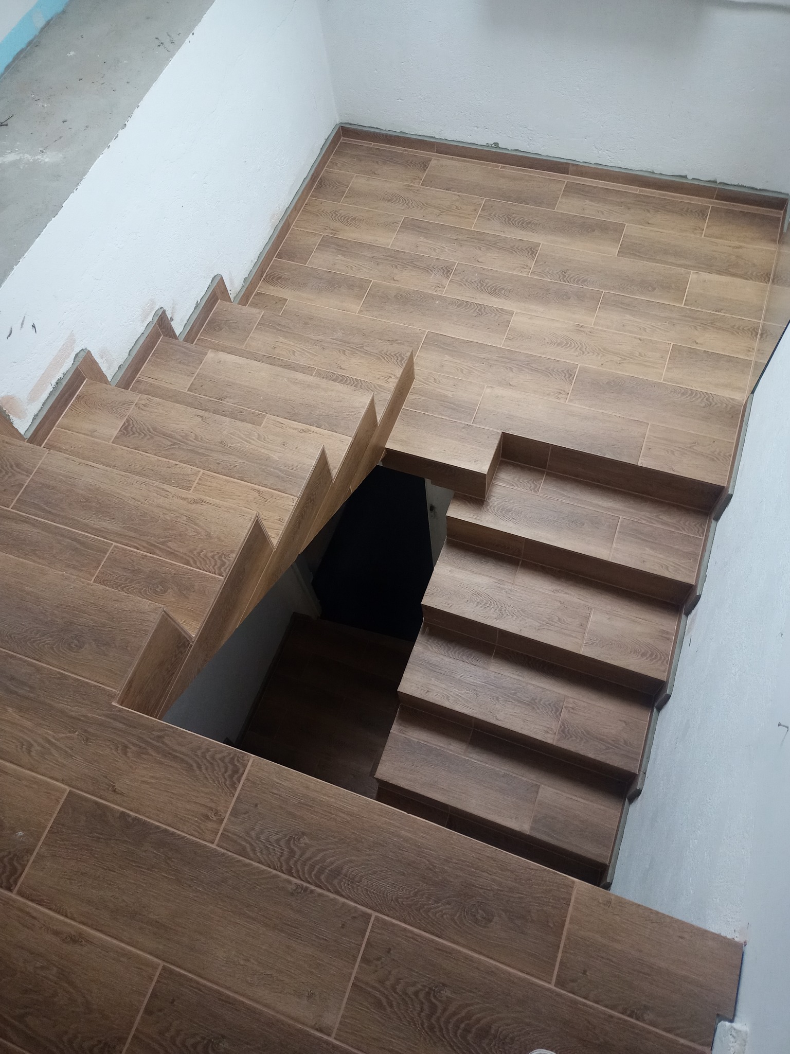 Wyłożone płytkami imitującymi drewno schody w dół, widok z góry, ściany częściowo wykończone.