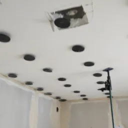 Montaż instalacji w suficie podwieszanym: widoczne okrągłe mocowania i częściowo odsłonięta konstrukcja w narożniku pomieszczenia.