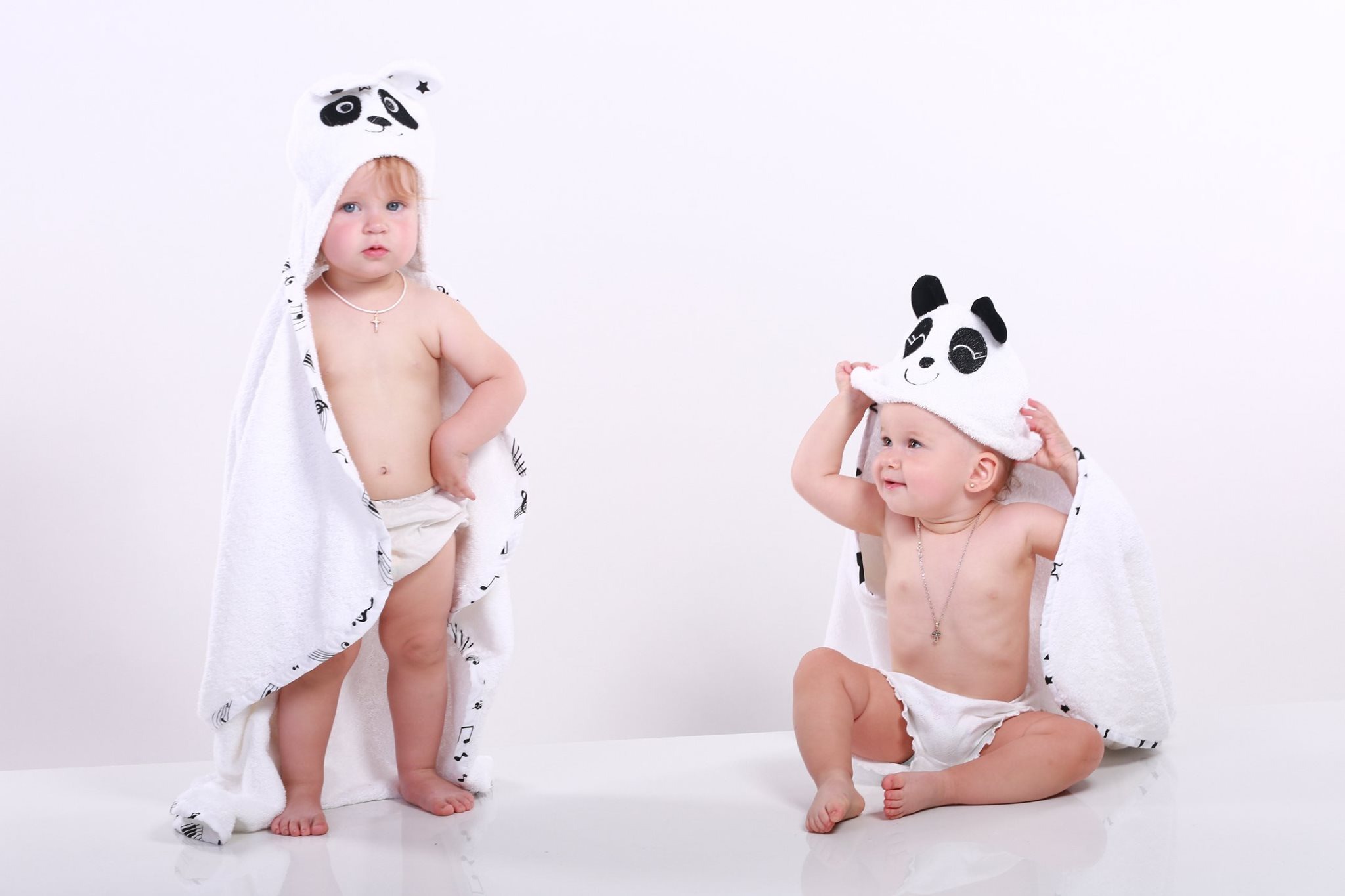 Dwoje małych dzieci w białych ręcznikach z kapturem w kształcie pandy na białym tle. Ręcznik jednego dziecka ma nadrukowane nuty.