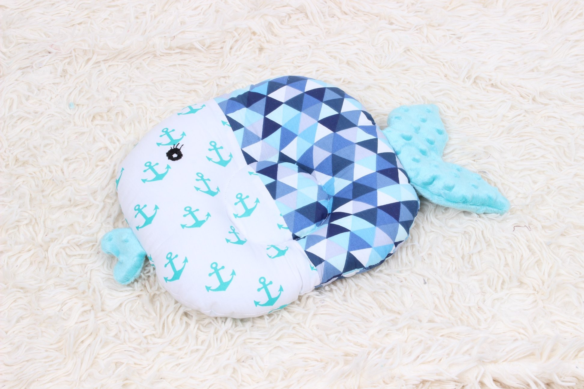 Poduszka w kształcie ryby z wzorem kotwic i trójkątów na białym puszystym tle.