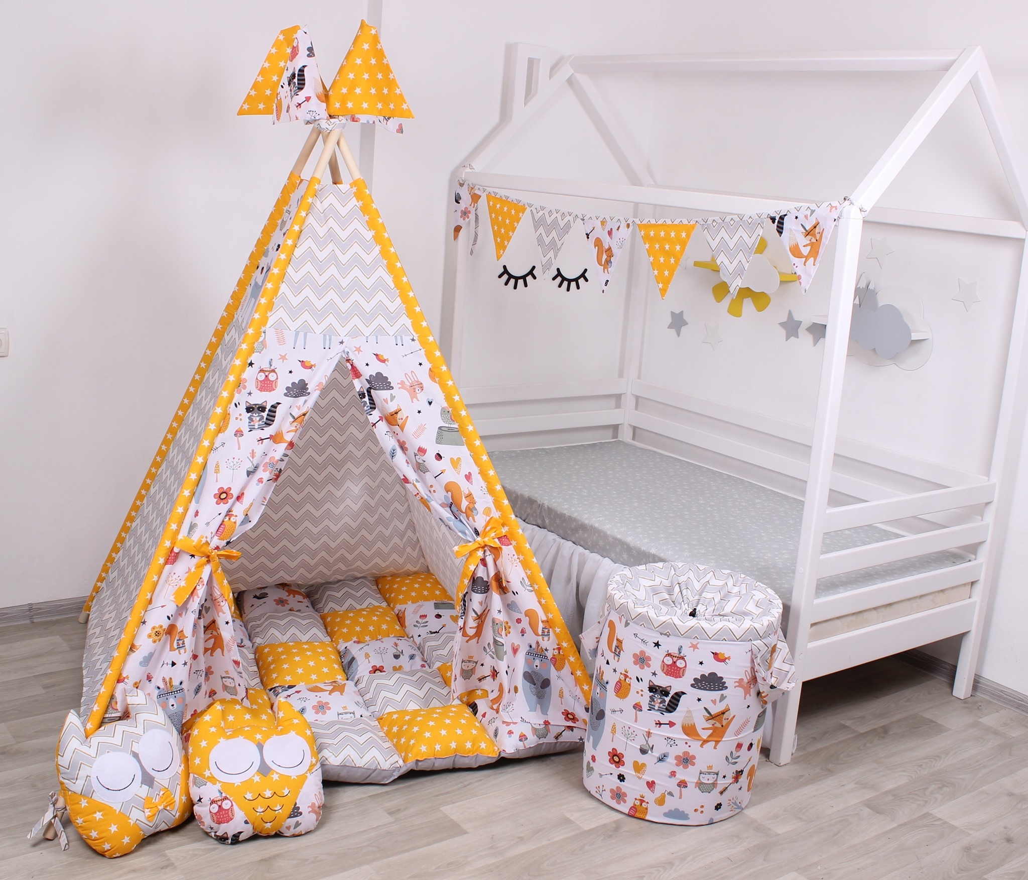 Pokój dziecięcy z białym łóżkiem w kształcie domku, tipi z szaro-żółtym wzorem w zygzaki i motywem leśnych zwierząt, poduszkami w kształcie sów i koszem na zabawki w tym samym stylu.