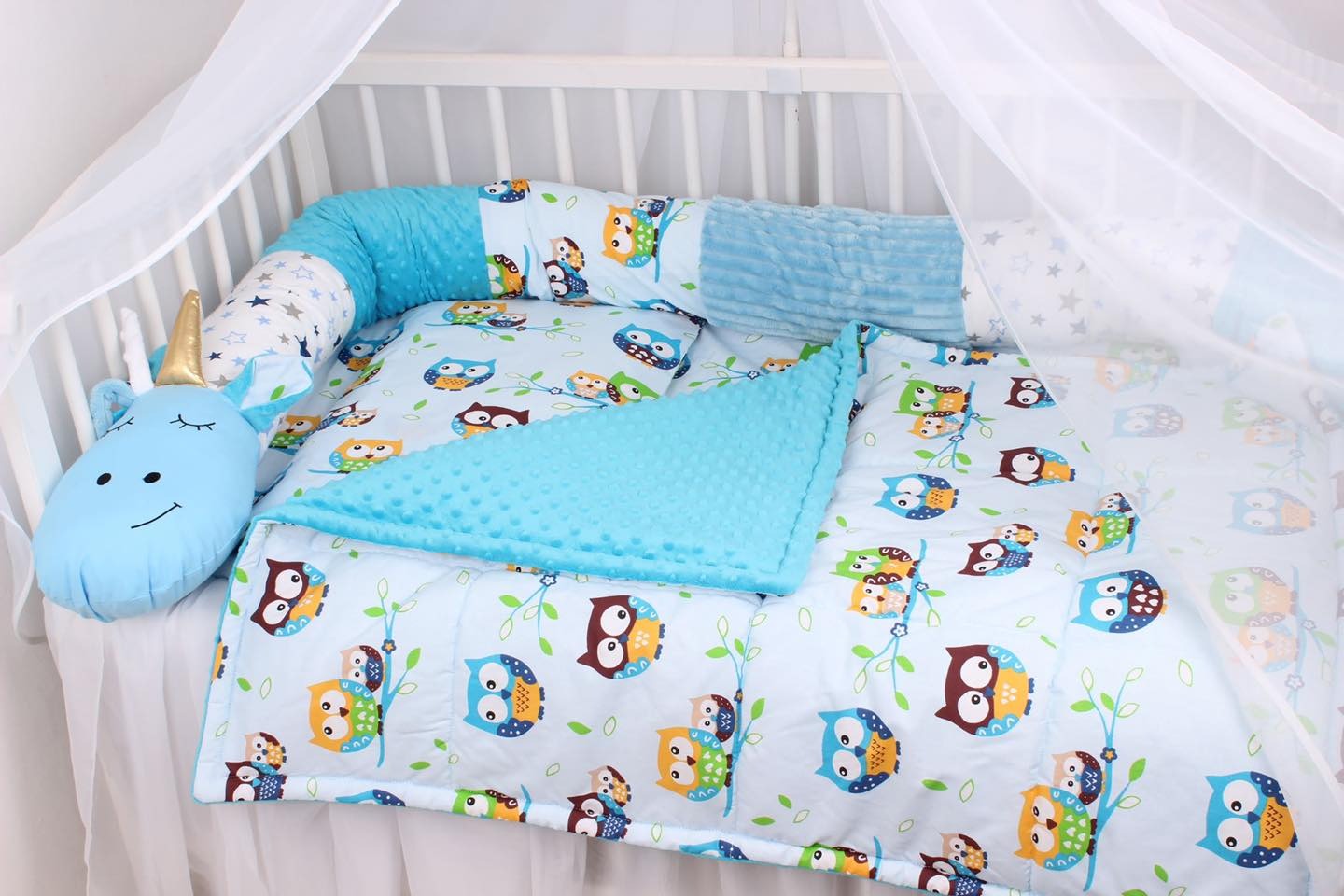 Dziecięce łóżeczko z baldachimem, wypełnione pościelą z motywem sów, poduszka-wałek z gwiazdkami i miękki pluszowy jednorożec z złotym rogiem.