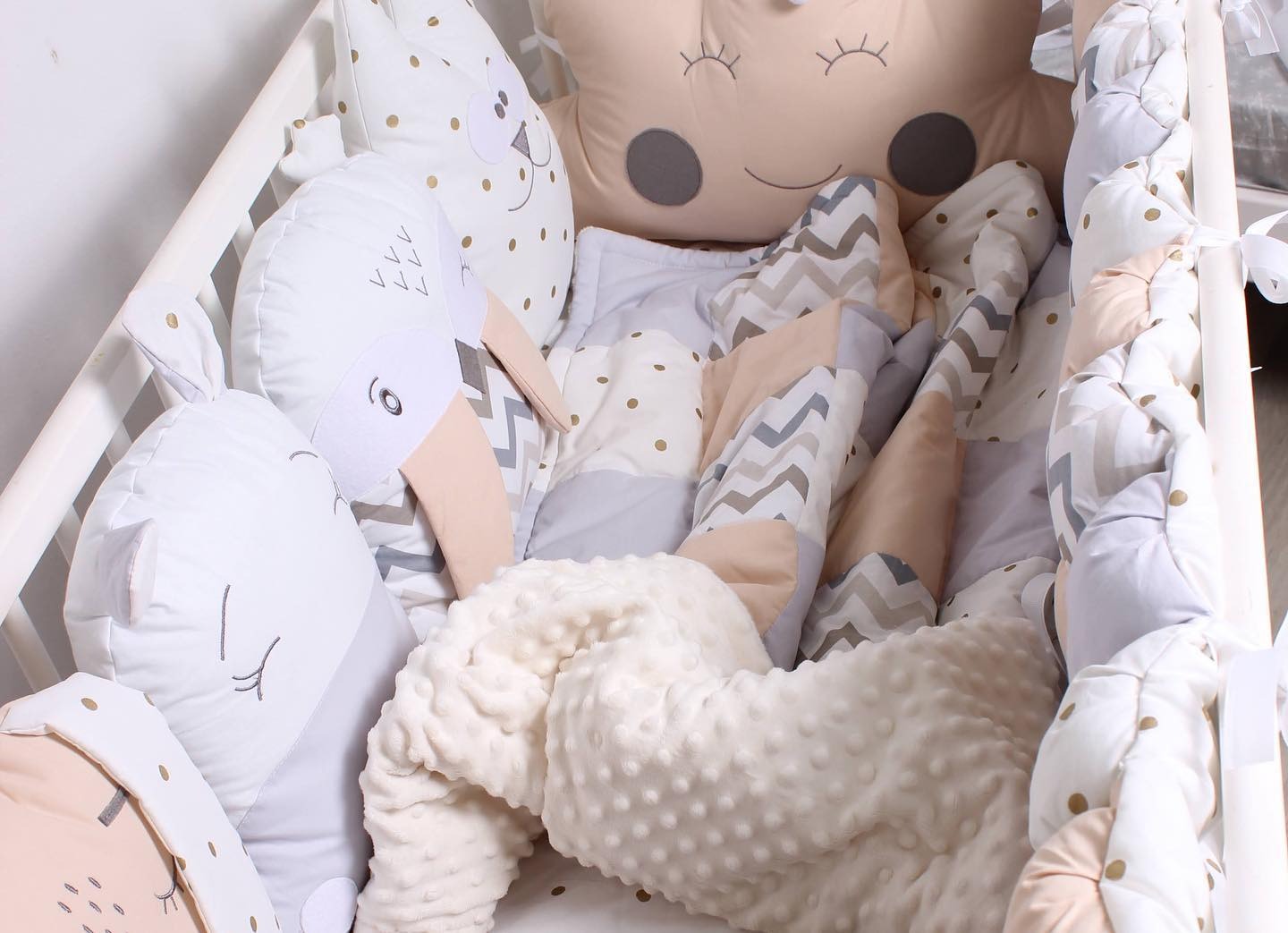 Wnętrze dziecięcego łóżeczka w Gdańsku wypełnione poduszkami dekoracyjnymi w kształcie zwierząt i chmurki, z patchworkową kołderką i miękkim ochraniaczem z wypustkami.
