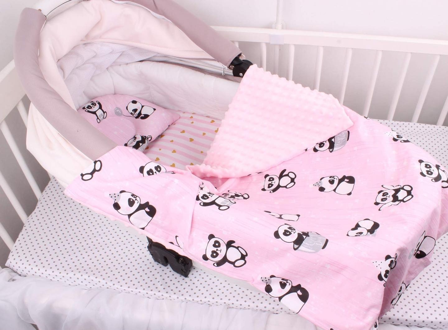 Różowa kołderka z motywem pandy włożona do dziecięcego łóżeczka, widoczna także poduszka z tym samym wzorem i fragment baldachimu.