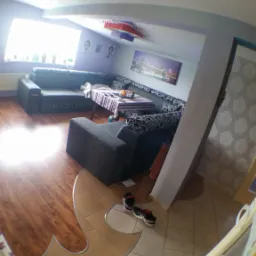 Pokój dzienny z narożną sofą, stolikiem, panelami podłogowymi i płytkami podłogowymi, sfotografowany obiektywem typu rybie oko.