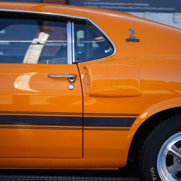 FOTOABERRACJA KAROL GACKOWSKI - Pomarańczowy samochód Shelby Mustang z czarnymi pasami bocznymi, widok z boku na drzwi i tylny błotnik, z kroplami wody na lakierze.