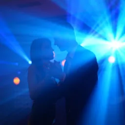 Sylwetki pary tańczącej w niebieskim świetle reflektorów na parkiecie. Mężczyzna w garniturze, kobieta w sukience. Dynamiczne ujęcie z imprezy.