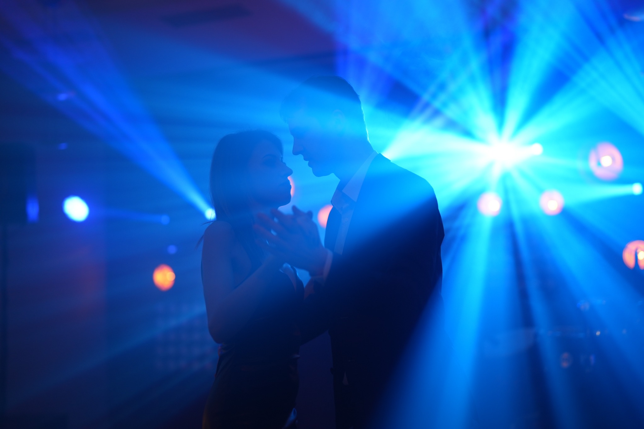 Sylwetki pary tańczącej w niebieskim świetle reflektorów na parkiecie. Mężczyzna w garniturze, kobieta w sukience. Dynamiczne ujęcie z imprezy.