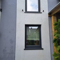 Blask Time - Dwukolorowa elewacja budynku po czyszczeniu, z dwoma oknami w czarnych ramach. Widoczne ślady po czyszczeniu na szarej części ściany.