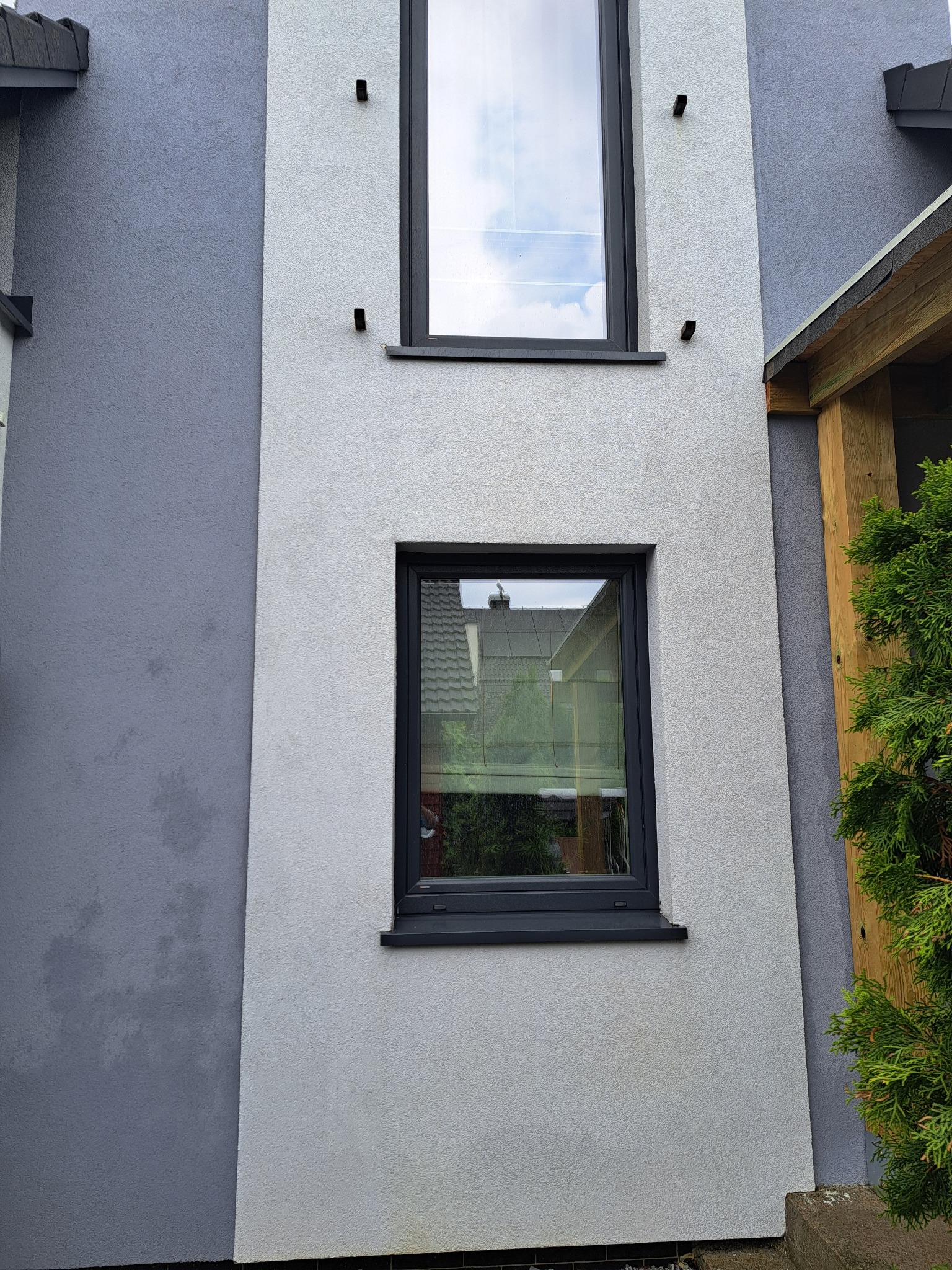 Dwukolorowa elewacja budynku po czyszczeniu, z dwoma oknami w czarnych ramach. Widoczne ślady po czyszczeniu na szarej części ściany.