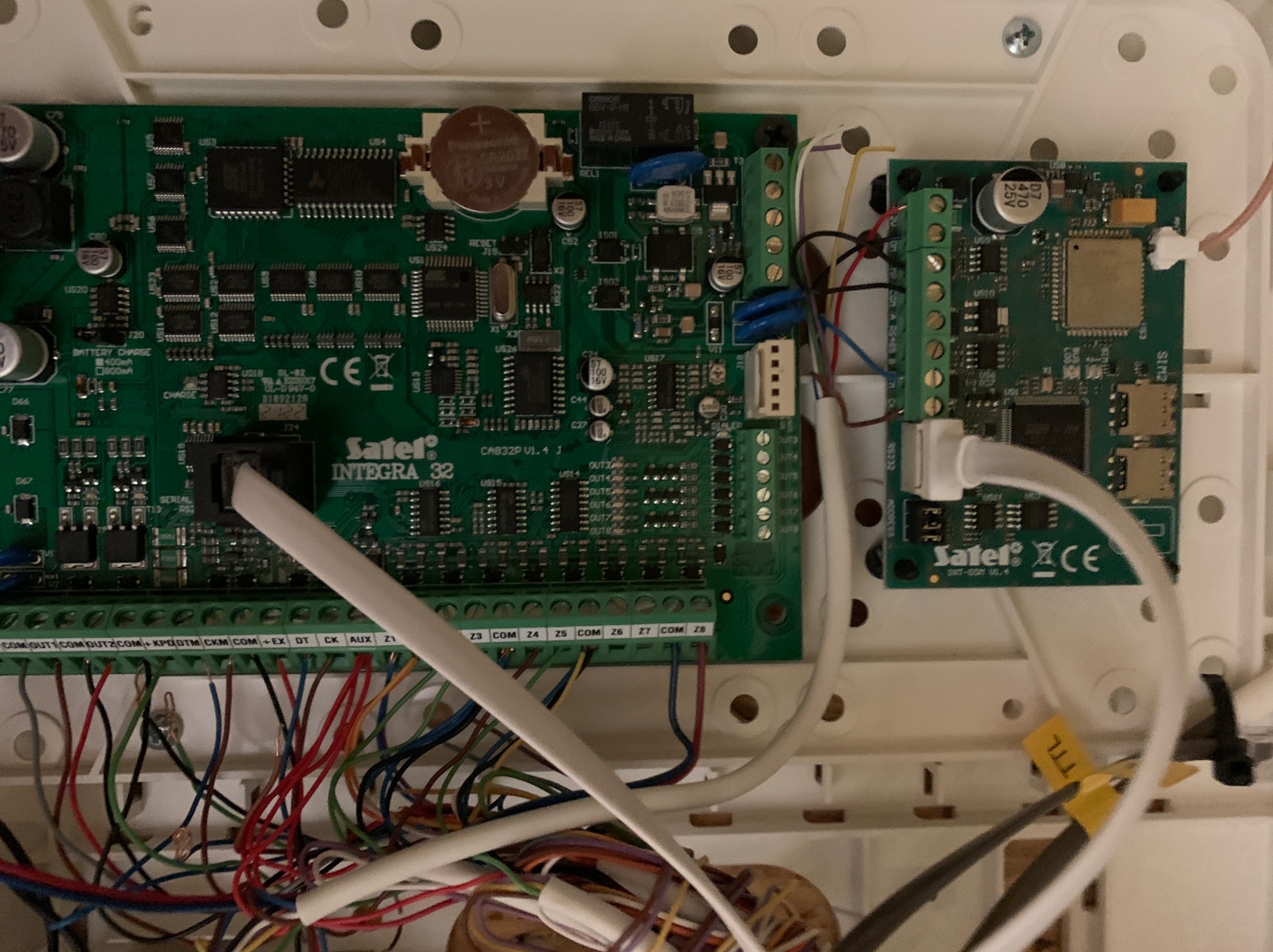 Centrala alarmowa Satel Integra 32 z modułem rozszerzeń, widoczne liczne połączenia kablowe i oznaczenia na płytkach drukowanych.
