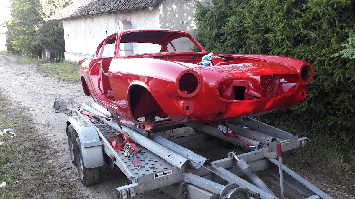 Czerwone nadwozie klasycznego samochodu bez szyb i reflektorów, umieszczone na lawecie transportowej, w trakcie renowacji.