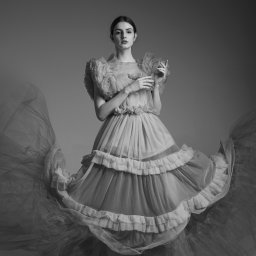 Adrianna Sołtys Fotografia - Portret kobiety w tiulowej sukni z falbanami, na szarym tle. Ujęcie studyjne, czarno-białe, z delikatnym światłem podkreślającym fakturę materiału.