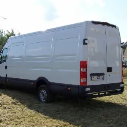 Biały samochód dostawczy marki Iveco, widok z tyłu, zaparkowany na trawiastym terenie, z widoczną tablicą rejestracyjną BI 8201G i słupami wysokiego napięcia w tle.