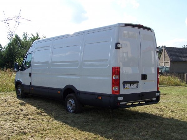 Biały samochód dostawczy marki Iveco, widok z tyłu, zaparkowany na trawiastym terenie, z widoczną tablicą rejestracyjną BI 8201G i słupami wysokiego napięcia w tle.