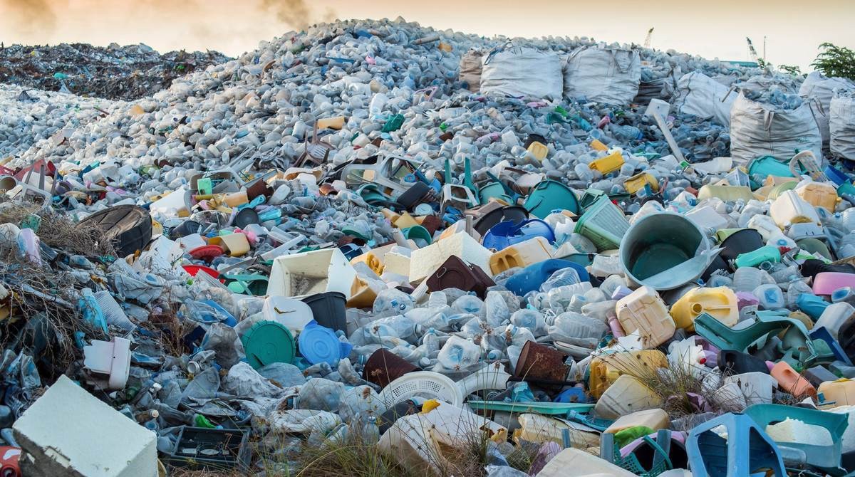 Ogromna góra różnorodnych odpadów plastikowych i gruzu, w tym butelki, pojemniki, fragmenty mebli i inne przedmioty, ukazana w dziennym świetle na składowisku.