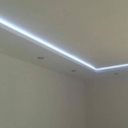 Firma Usługowa Złota Rączka Piotr Mikulewicz - Biały sufit z oświetleniem LED wzdłuż krawędzi, minimalistyczny design, widoczne punkty świetlne i włączniki na ścianie. Nowoczesne wykończenie wnętrza.