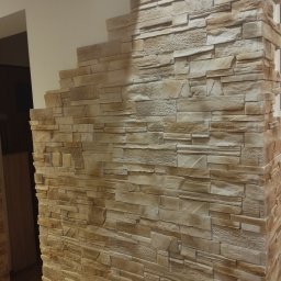 Firma Usługowa Złota Rączka Piotr Mikulewicz - Ściana wykończona dekoracyjnym kamieniem w odcieniach beżu i brązu, z widocznymi włącznikami światła. Imitacja kamiennej ściany wewnątrz pomieszczenia.