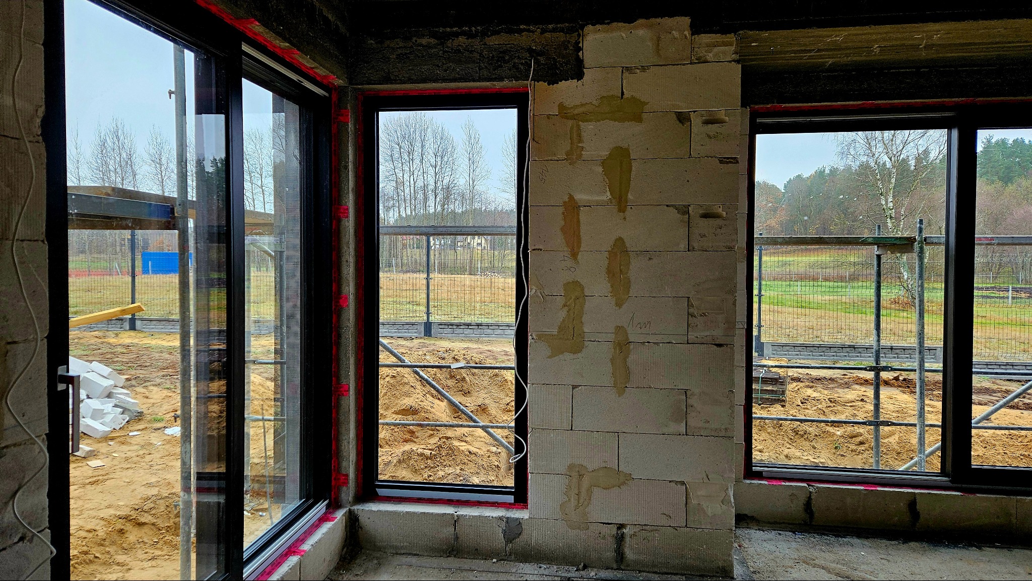Montaż okien PCV w surowym wnętrzu budynku w Gostkowie, widoczne bloczki betonowe i wstępnie osadzone ramy okienne z widokiem na zewnątrz.