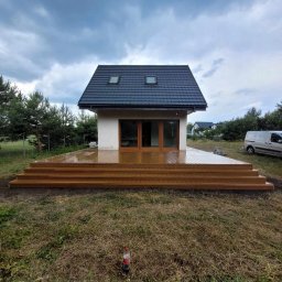 P-M Tarasy - Nowoczesny dom z dużym, drewnianym tarasem schodkowym, widok z poziomu trawy, pochmurne niebo.