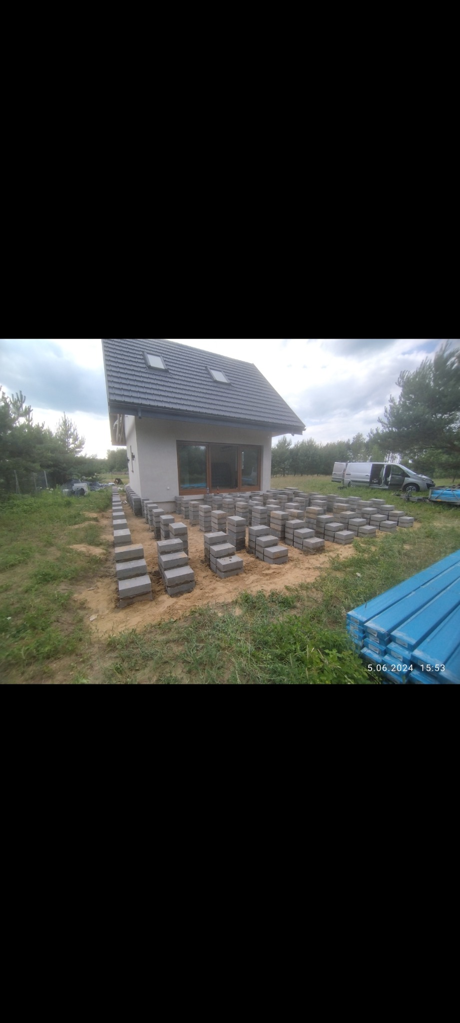 Przygotowanie podłoża pod taras betonowy: ułożone kostki betonowe na piasku, w tle nowoczesny dom z szarym dachem i widoczny samochód dostawczy.