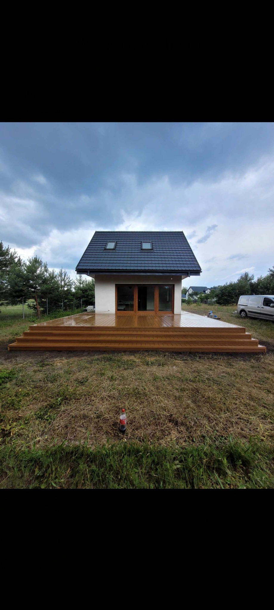 Nowoczesny dom z dużym, drewnianym tarasem schodkowym, widok z poziomu trawy, pochmurne niebo.