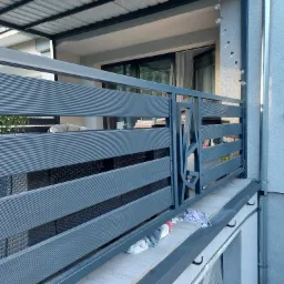 Nowoczesna balustrada balkonowa z poziomych profili, szara, z widocznymi śladami montażu i narzędziami na podłodze balkonu, zadaszony balkon z oknami w tle.